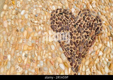 Die Textur der Steinmauer, die Straße aus kleinen runden und ovalen Steinen mit abstrakten Herzmustern sandige Nähte von natürlichem, altgelbem Bla Stockfoto