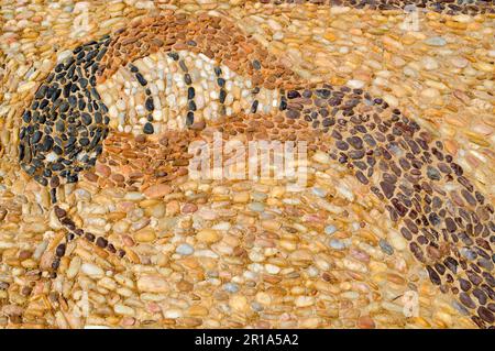 Die Textur der Steinmauer, die Straße aus kleinen runden und ovalen Steinen mit abstrakten Linien von Schlangenmustern mit sandigen Nähten von natürlichem altem Yello Stockfoto