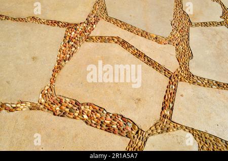 Textur einer Steinmauer, Straßen aus Steinen, Ziegel, Kopfsteinpflaster, Fliesen mit sandigen Nähten aus grauem, altem Gelb mit scharfen Kanten. Hinten Stockfoto