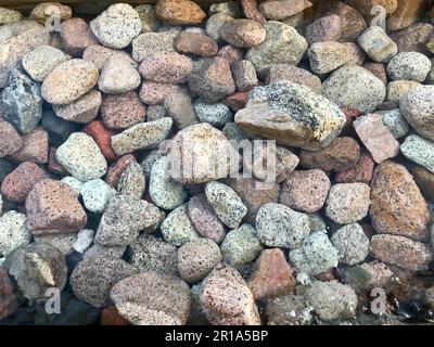 Eine wunderschöne Textur aus mehrfarbigen runden und ovalen Natursteinen, Felsbrocken, Kopfsteinpflaster unter dem blauen Wasser, Unterwasserblick auf das Meer Stockfoto