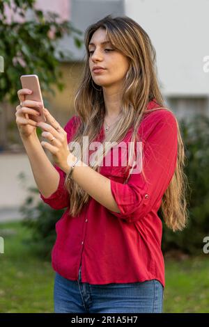 Porträt einer jungen blonden Frau, die ihr Smartphone im Freien benutzt. Modernes Technologiekonzept Stockfoto