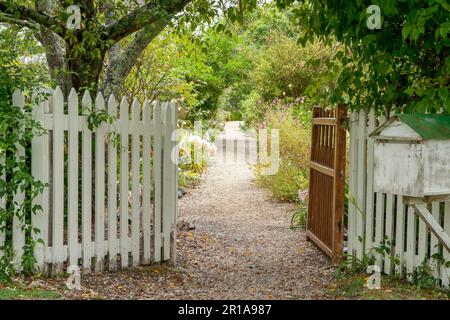 Schotterpfad führt zwischen Schlepptüren, eingezäunt durch alten englischen Garten mit wilden und kultivierten Blumen und Bäumen. Stockfoto