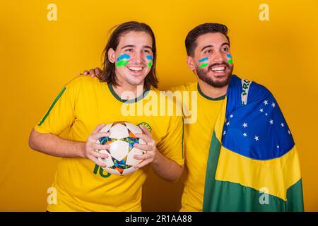 Brasilianische Freunde, lateinamerikaner, Vielfalt, Brasilien anfeuern, bei der Weltmeisterschaft 2022, Ball und Flagge halten, aufmerksam auf das Spiel, glücklich Stockfoto