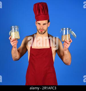 Professioneller Koch mit Kochmütze und Schürze hält Glasgefäße mit Grobgrieß und Müsli. Frühstück und gesunde Ernährung. Körnung, Grobgrieß, Bio-Lebensmittel und Stockfoto