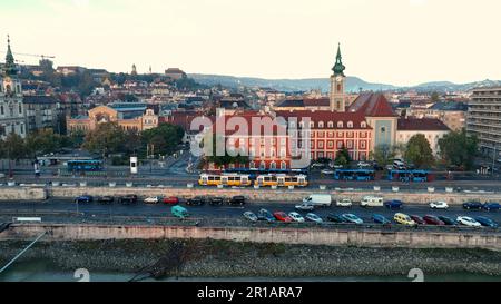 Typische Budapester Straßenbahn, die durch das Stadtviertel im wunderschönen goldenen Licht des Sonnenaufgangs fährt, Luftverfolgung, Folgeschuss Weitwinkel Stockfoto
