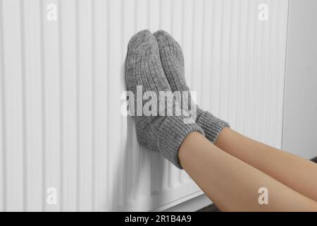 Frau wärmt Beine auf Heizkörper nahe weißer Wand, Nahaufnahme Stockfoto