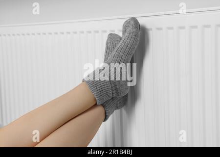 Frau wärmt Beine auf Heizkörper nahe weißer Wand, Nahaufnahme Stockfoto