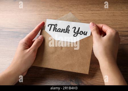 Frau mit Umschlag und Karte mit Phrase Danke am Holztisch, Nahaufnahme Stockfoto