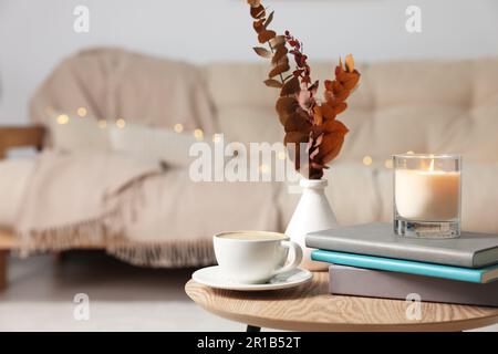 Brennende Kerze, Tasse und Bücher auf einem hölzernen Couchtisch im Zimmer. Platz für Text Stockfoto