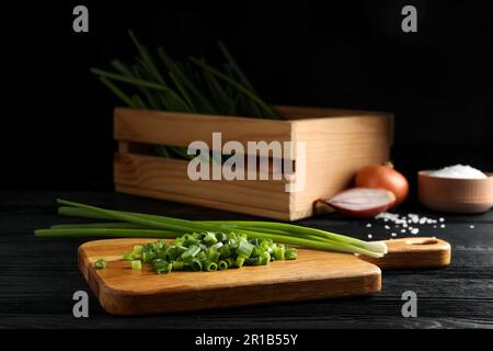 Gehackte grüne Frühlingszwiebeln und Stiele auf schwarzem Holztisch Stockfoto