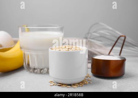 Verschiedene Zutaten zum Kochen leckerer Haferflocken-Pfannkuchen auf grauem Tisch Stockfoto