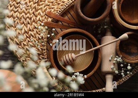 Holzschüsseln, Walznadel und Honigstiel in der Nähe von Blumen auf Korbmatte, flach liegend Stockfoto