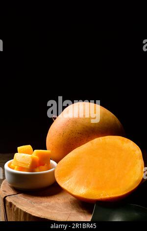 Mango- und Mangoscheiben mit Würfeln auf schwarzem Hintergrund. Thailändische Mangos. Thailändische Früchte. Text kopieren. Platz kopieren. Stockfoto