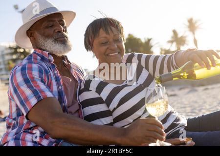 Glückliches Senior-afroamerikanisches Paar mit Picknick und Wein am Strand Stockfoto