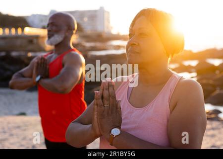 Glückliches Senior-afroamerikanisches Paar, das Yoga praktiziert und am Strand posiert Stockfoto