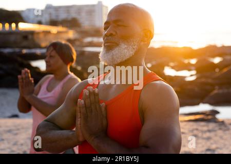 Glückliches Senior-afroamerikanisches Paar, das Yoga praktiziert und am Strand posiert Stockfoto