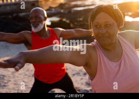 Glückliches Senior-afroamerikanisches Paar, das Yoga praktiziert und am Strand posiert Stockfoto