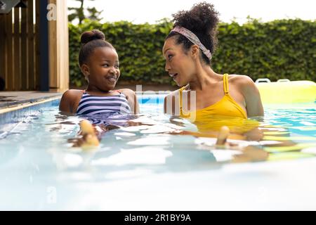 Glückliche afroamerikanische Mutter und Tochter, die sich im Pool unterhalten Stockfoto