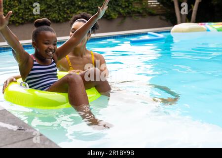 Glückliche afroamerikanische Mutter und Tochter, die mit dem aufblasbaren Becken im Schwimmbad spielten, Kopierbereich Stockfoto