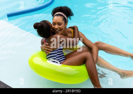 Frohe afroamerikanische Mutter und Tochter auf aufblasbaren Umarmungen im Swimmingpool Stockfoto