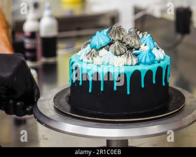 Der Koch bereitet einen mattierten, schwarz bemalten Tassenkuchen mit blauem Türkis und einem farbigen, handgemachten Baiser-Belag zu Stockfoto