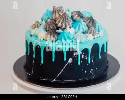 Mattschwarzer Tassenkuchen mit blau-türkisfarbenem, tropfendem Hintergrund und farbiger handgemachter Baiser-Garnitur im Studio mit isoliertem, weißem Hintergrund Stockfoto