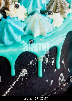 Mattschwarzer Tassenkuchen mit blau-türkisfarbenem, tropfendem Hintergrund und farbiger handgemachter Baiser-Garnitur im Studio mit isoliertem, weißem Hintergrund Stockfoto