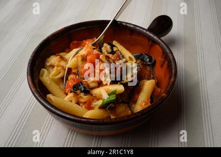 Pasta alla Norma oder Penne Rigate mit Auberginen- und Tomatensoße und Ricotta in einer rustikalen Terrakotta-Schüssel Stockfoto