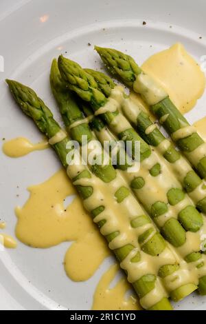 Grüner Spargel mit Sauce Hollandaise, serviert auf einem weißen Teller Stockfoto