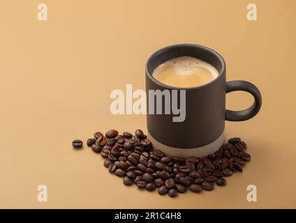 Kaffeebohnen mit einer Tasse heißem, cremigen schwarzen Kaffee auf beigefarbenem Brett Stockfoto