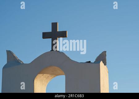 Ein Kreuz auf der Spitze einer orthodoxen, weiß getünchten Kirche in iOS Griechenland und ein blauer Himmel im Hintergrund in iOS Griechenland Stockfoto