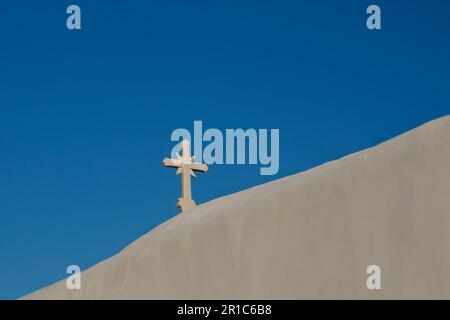 Ein Kreuz auf der Spitze einer orthodoxen, weiß getünchten Kirche in iOS Griechenland und ein blauer Himmel im Hintergrund in iOS Griechenland Stockfoto