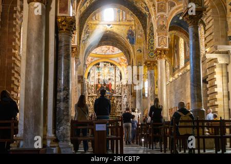 Die Leute gehen zur Messe in der Kirche, ein Sonnenstrahl tritt durch ein Fenster ein. Byzantinische und barocke Kirche St. Mary vom Admiral, Martorana. Palermo Stockfoto