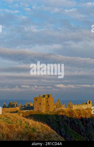 Dunnottar Castle in der Nähe von Stonehaven an der Ostküste Schottlands mit seinen zerstörten Gebäuden, die von der goldenen untergehenden Sonne erfasst wurden. Stockfoto