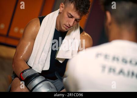 Attraktiver junger, schwitzender Boxspieler, der nach dem Spiel in der Garderobe sitzt. Sport, Lifestyle, Gesundheitskonzept. Stockfoto
