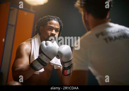 Junger schwitzender Boxspieler, der nach dem Training mit dem Trainer sitzt. Ich fühle mich mächtig. Sport, Lifestyle-Konzept. Stockfoto