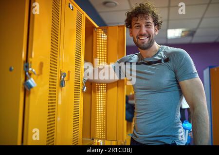 Fröhlicher junger Mann, der im Umkleideraum des Fitnessstudios steht und sich auf das Training vorbereitet. Gesundheit, Lifestyle-Konzept. Stockfoto