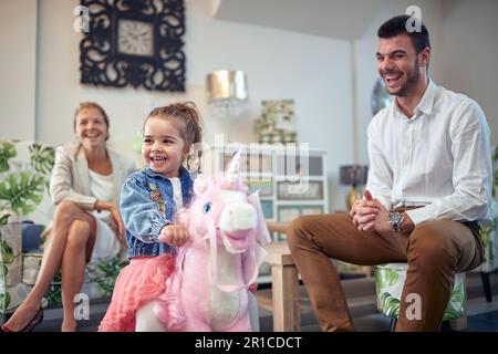 Glückliche Familie wird gefangen in einem Moment reiner Freude und Glück. Man kann die Mutter im Hintergrund lachen sehen, während der Vater neben dem steht Stockfoto