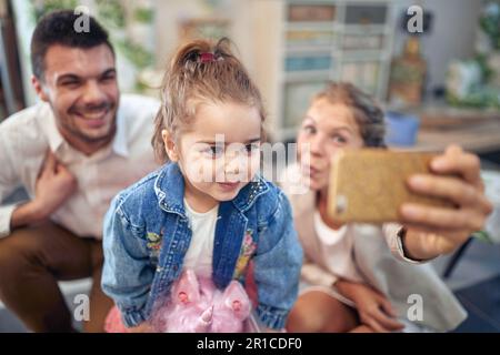 Der besondere Moment der Familie, zusammen ein Selfie zu machen. Mutter, Vater und ihre Tochter stehen sich nahe, mit einem großen Lächeln im Gesicht. Der mothe Stockfoto