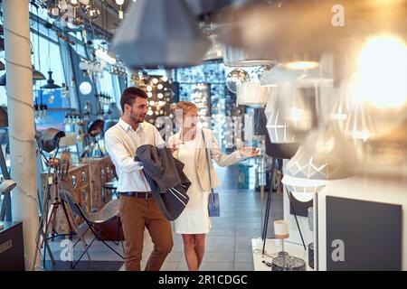 Ein glückliches Paar sieht sich in einem Möbelgeschäft eine Vielzahl von Lampen und Lampen an. Stockfoto