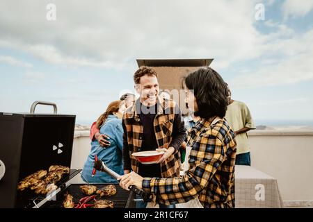 Glückliche, generationenübergreifende Menschen, die Spaß beim Grillen auf dem Dach des Hauses haben - Sommerversammlungen und Essenskonzept Stockfoto