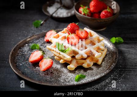 Hausgemachte und frische Waffeln mit Puderzucker und Beeren. Sommerdessert mit Erdbeeren. Stockfoto