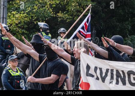 Neonazis-Demonstranten mit Flaggen salutieren, da sie während der Demonstration das Gebiet verlassen sollen. Ein Tag politischer Spannungen und Zusammenstöße entfaltete sich in Melbourne als rechtsextreme Gruppe einer Neonazi-Gruppe, die eine Anti-Einwanderungs-Kundgebung im staatsparlament veranstaltete, und traf auf heftigen Widerstand von linksgerichteten antifaschistischen Gegenprotestierenden. Die Aufruhr-Polizei wurde eingesetzt, als es zwischen den beiden Gruppen zu Schlägereien kam, mit Pfefferspray und Pferden, um die Menge zu kontrollieren. Protestsignale, die Inklusivität, Vielfalt und soziale Gerechtigkeit fordern, wurden in einer Demonstration der Einheit gegen Hassreden und Diskriminierung hoch gehalten. Die Überschneidung Stockfoto
