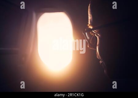 Porträt des Menschen im Flugzeug. Selektiver Fokus auf Passagier während des Fluges beim Sonnenuntergang durch das Fenster. Stockfoto