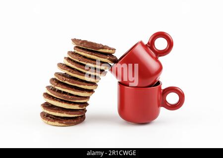 Gestapelte Schokoladenkekse, die sich in zwei rote Espressobecher lehnen Stockfoto