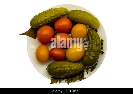 Eingelegte gelbe und rote Tomaten mit grünen Gurken auf einem weißen Teller Stockfoto