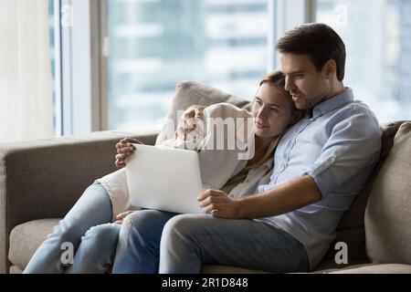 Positives, attraktives junges Paar, das zusammen einen Laptop benutzt Stockfoto