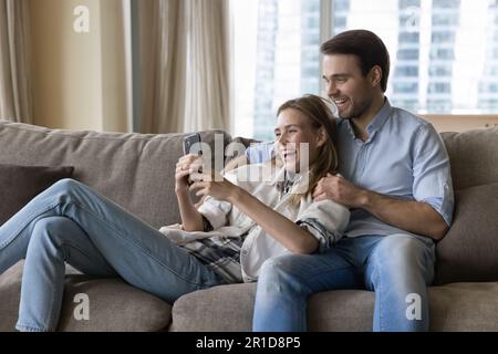 Fröhlicher junger Mann und Frau, die sich zu Hause umarmen und entspannen Stockfoto