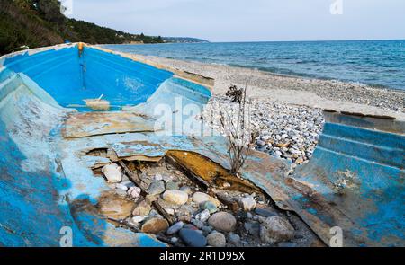 Ein verlassenes, kaputtes Boot voller Löcher, das in der Nebensaison am Meer lag Stockfoto