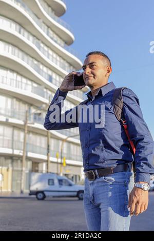 Junger Latino-Mann in einer Stadt, der ein Handy benutzt. Stockfoto